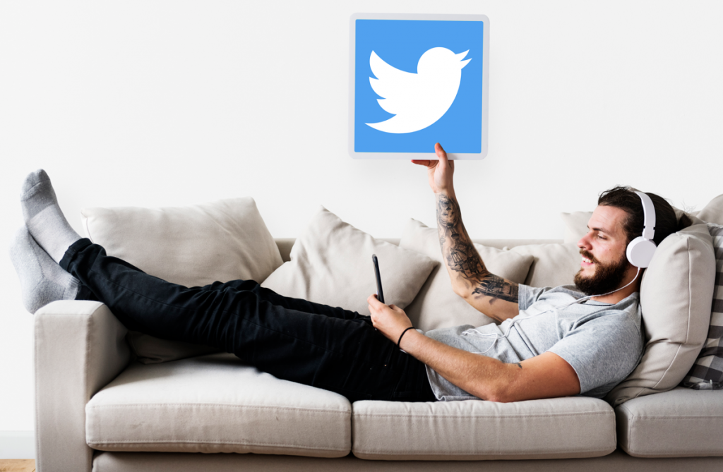 Um homem deitado em um sofá com fones de ouvido, segurando um telefone e um logotipo do Twitter acima dele.